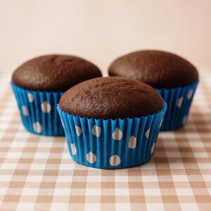 Three domed chocolate muffins in blue polka-dot cases on a gingham cloth