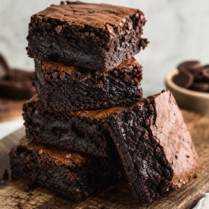 Stack of classic fudgy chocolate brownies with crackly tops on a wooden board