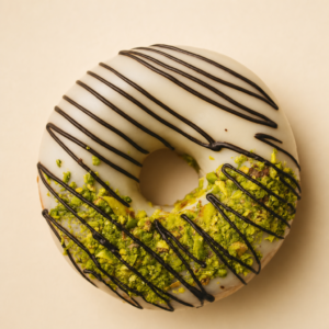 Ring donut with white icing, dark chocolate drizzle and crushed pistachios on a cream background
