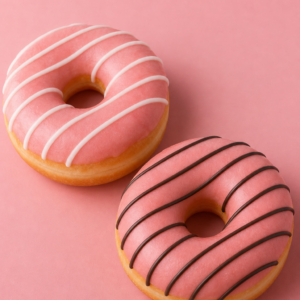 Two ring donuts with pink strawberry glaze and icing drizzle on a pink background
