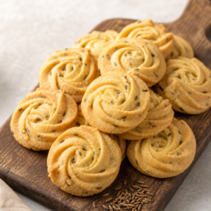Piped rosette jeera cumin butter cookies on a wooden board with roasted cumin seeds